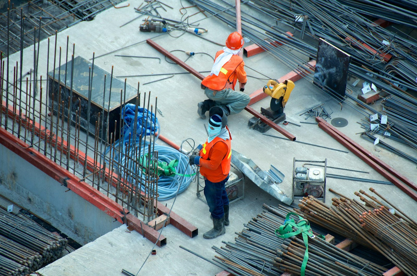 Two builders in orange workwear on a concrete deck beside stacked reinforcing steel